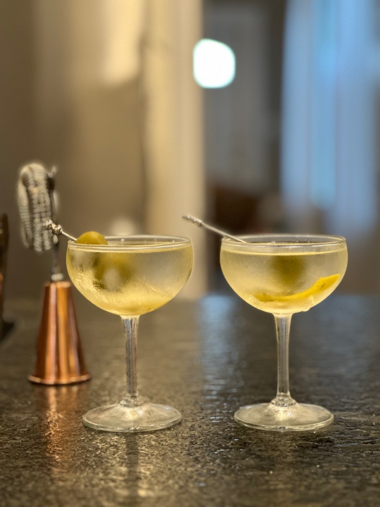 Two gin martinis. One has bleu cheese olives, the other with a twist.
